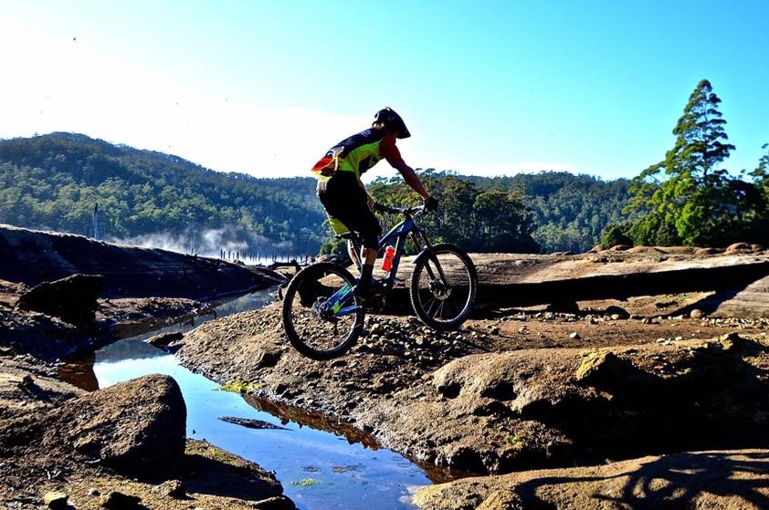 Mountain biker jumping a creek with hills and trees in the background.