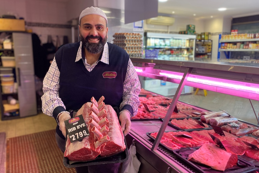 a man holding a tray of meat in a halal butcher