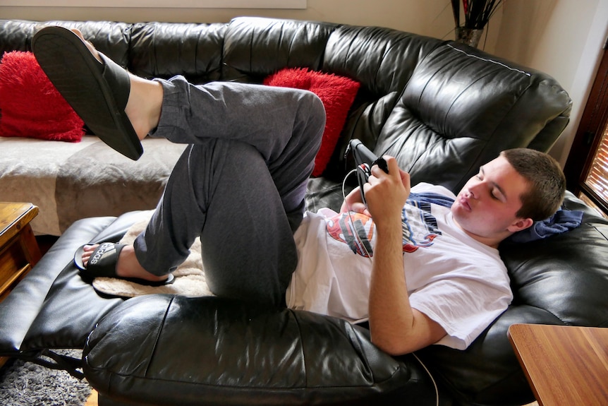 Boy in white shirt lying on black couch with ipad in his hands.