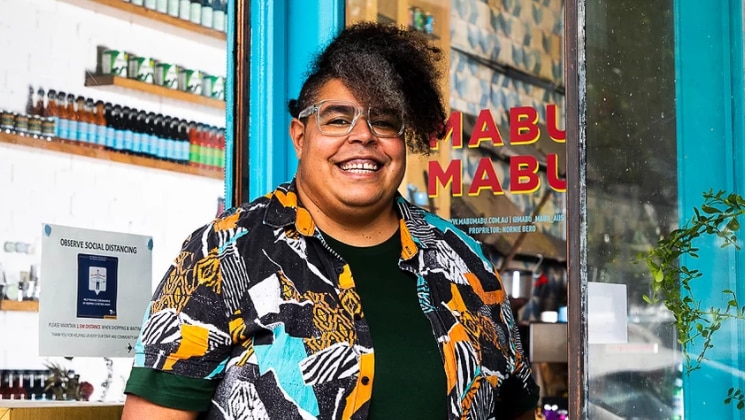 A Torres Strait Islander stands outside her restaurant, smiling.