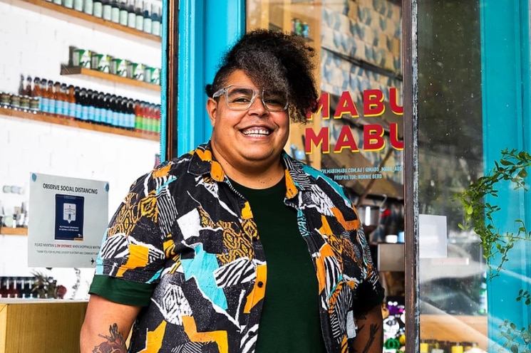 A Torres Strait Islander stands outside her restaurant, smiling.