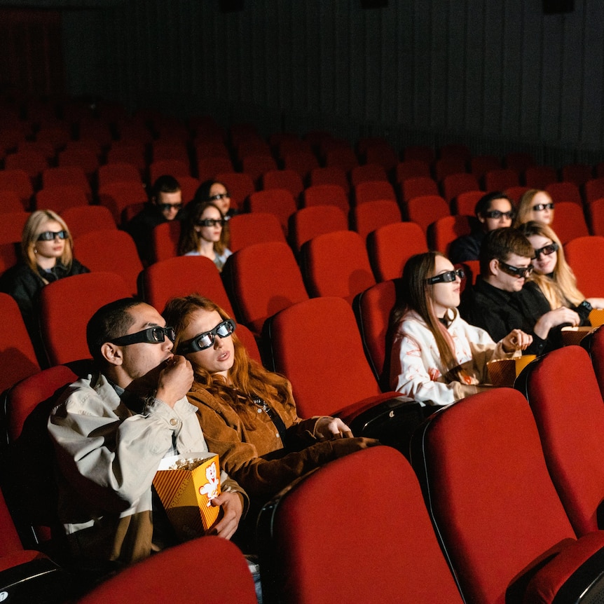 people scattered throughout a cinema in red chairs eating popcorn and drinks 