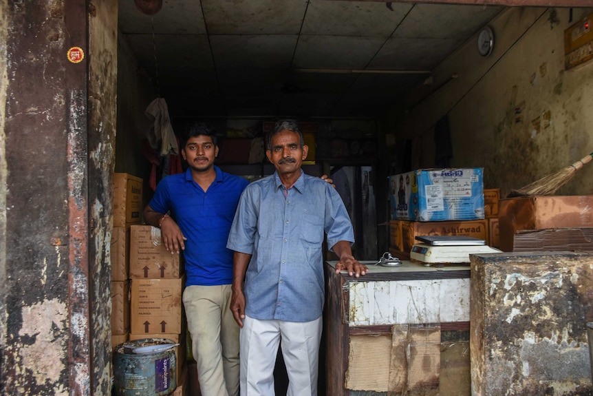 Two men standing inside a room with their arms around one another