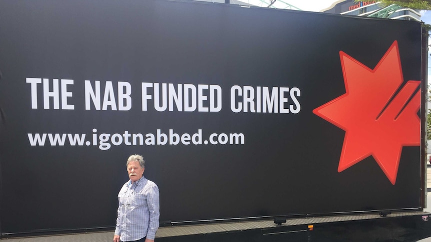 A man standing in front of a black billboard reading "The NAB funded crimes"