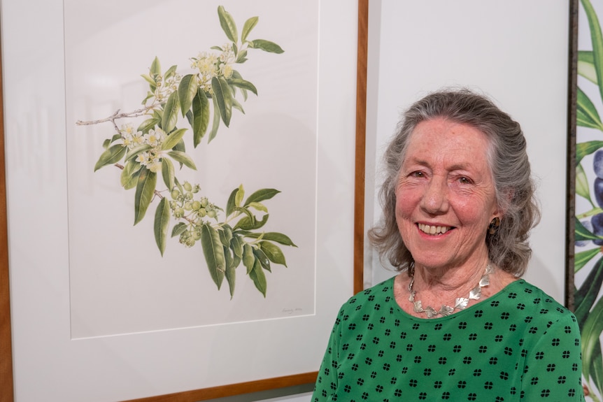 A woman smiles standing next to a painting of a plant.