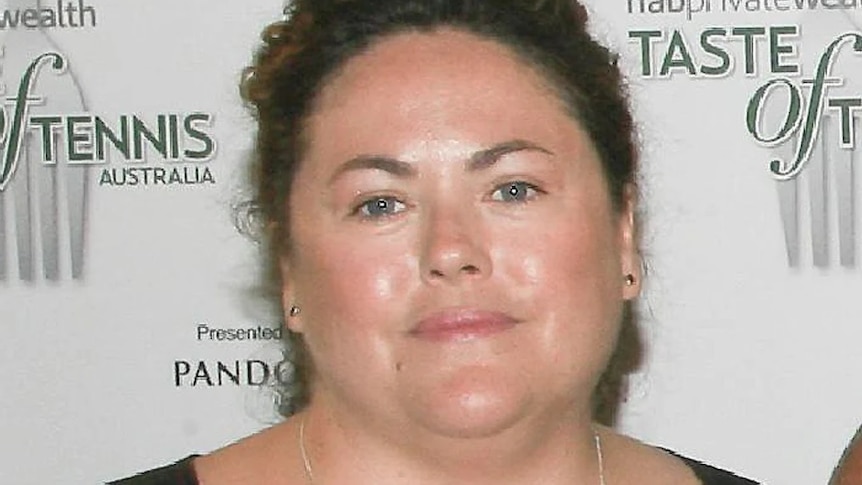 A woman standing in front of a promotional tennis sign.