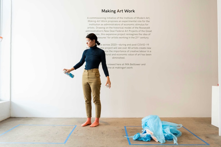 The artist Merinda Davies spraying disinfectant into a blue square, a pile of PPE in another blue square, during a performance