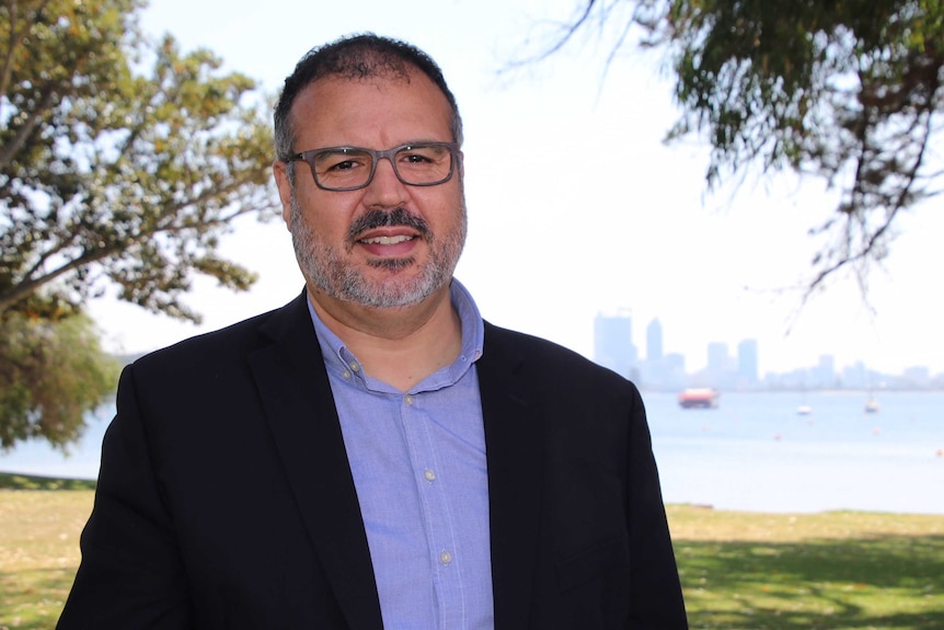 A head and shoulders shot of UWA water expert Anas Ghadouani smiling and standing in front of the Swan River.