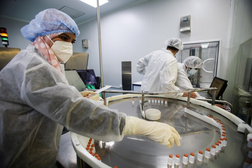 A woman in scrubs touches vials in a big metal drum 