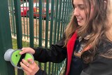A young girl locks her phone into a pouch on a school railing