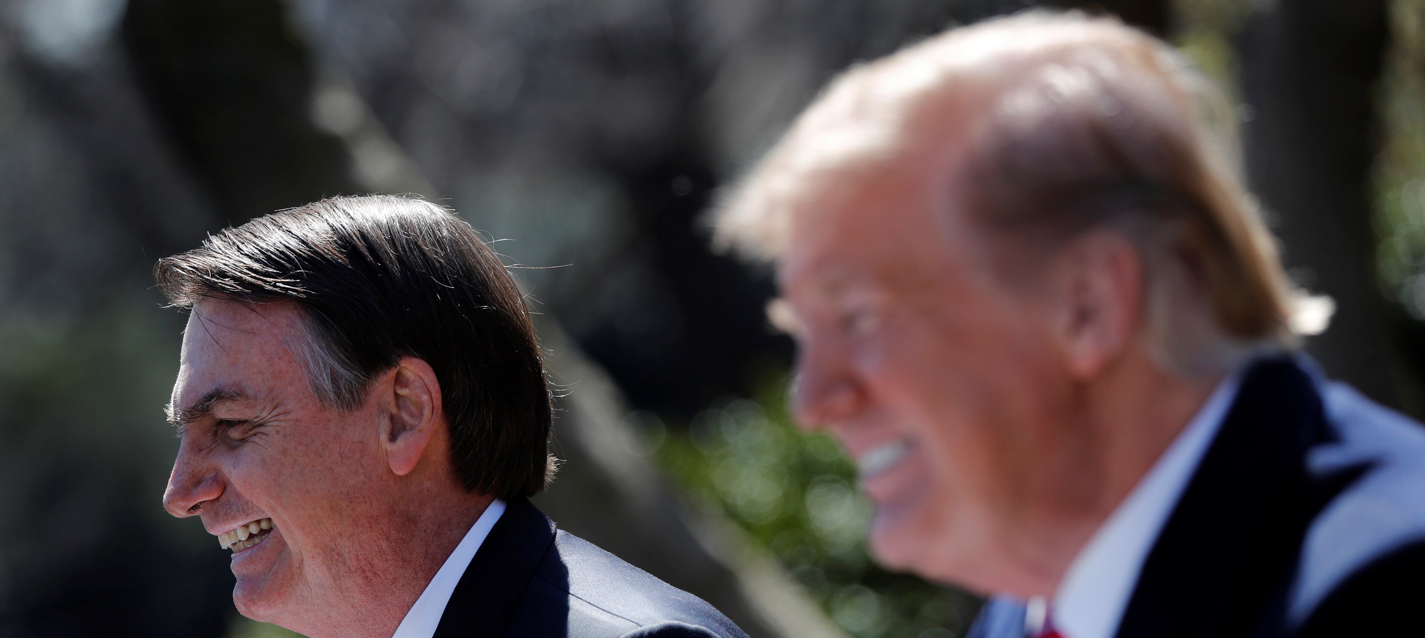 Donald Trump and Jair Bolsonaro, wearing extremely similar grinning facial expressions, stand near each other
