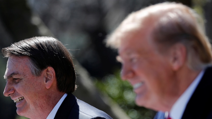 Donald Trump and Jair Bolsonaro, wearing extremely similar grinning facial expressions, stand near each other