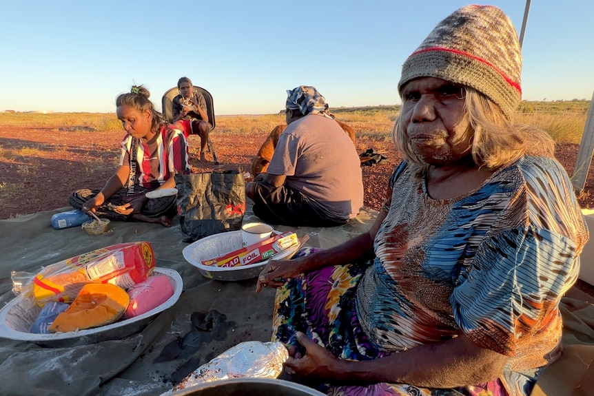 An Indigenous woman sits on the ground at sunset. 