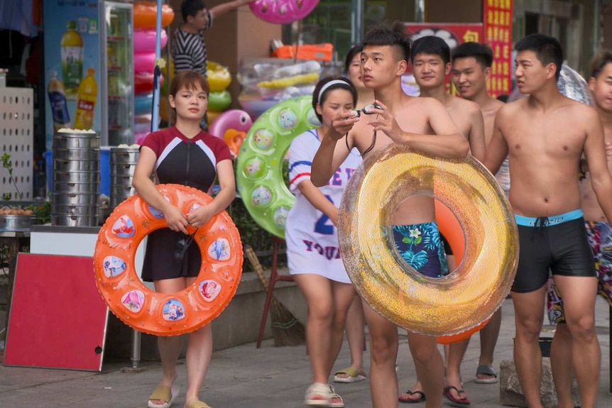 A group of young people with pool toys walking down a street