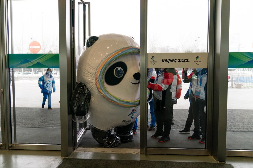 People stand around as a big panda bear mascot tries to fit through a door sideways
