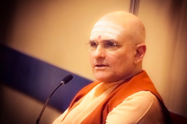 Wearing glasses and a red dot on his forehead, Russell Kruckman speaks into a microphone.