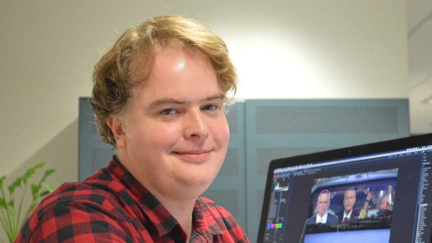 Parkinson smiling to camera with computer screen with one of his projects being edited in background.