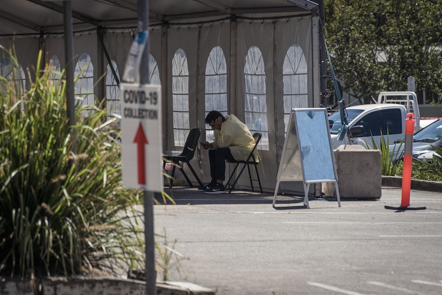 A worker sits at an empty COVID-19 testing clinic in Avalon reading his phone.