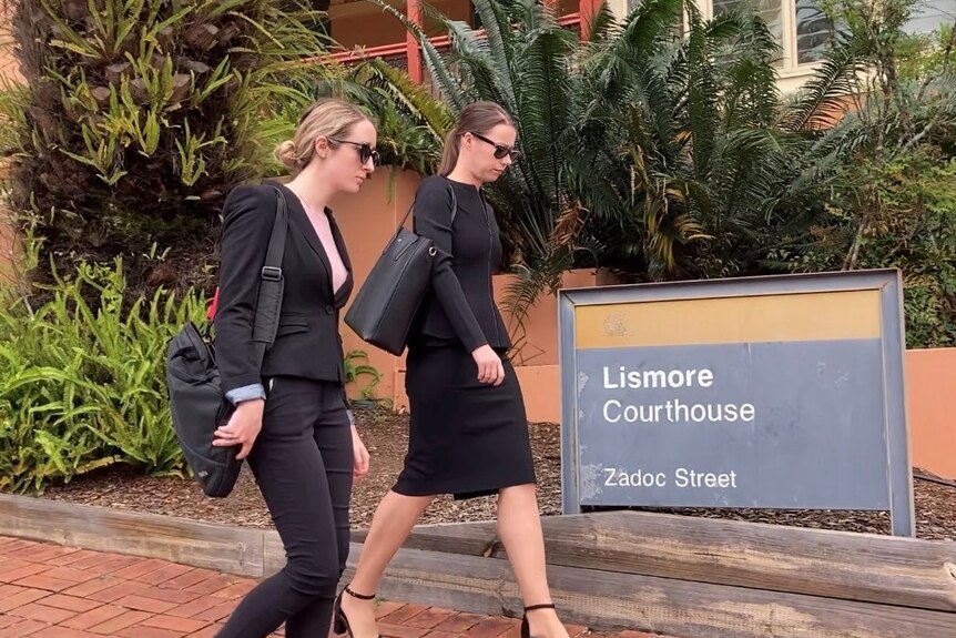 Two women in black business clothes walking on a path in front of a court house.
