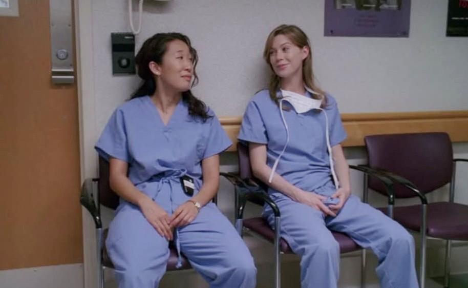 Dos mujeres vestidas con una bata azul se sientan en un banco de un hospital y se miran.