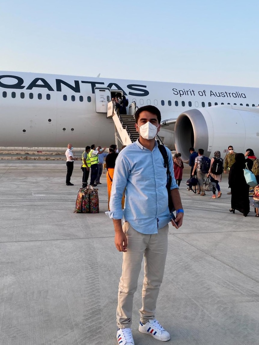 A young man wearing a mask in front of a Qantas plane