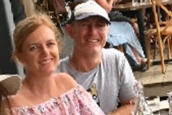 A couple smiling with their arms around one another at a restaurant.