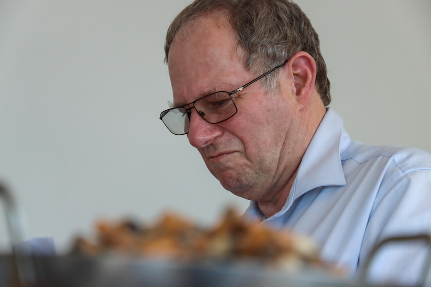 A man sits at a desk looking uphappy. In front of him is cigarettes. 