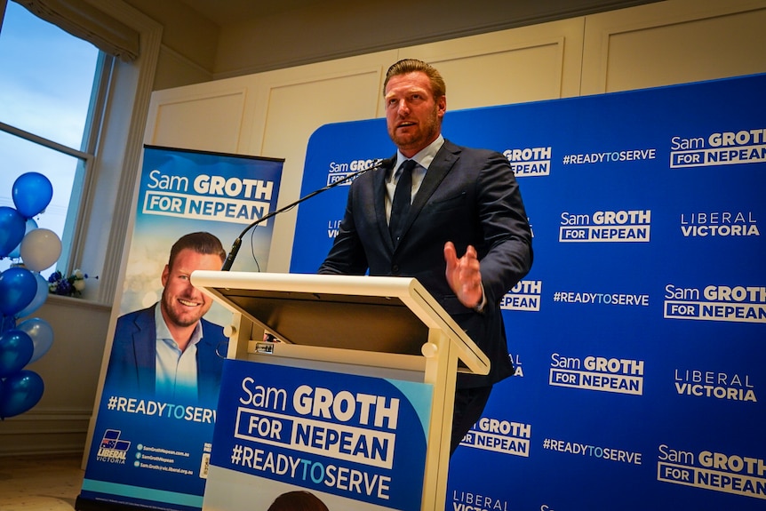 A man in his 30's wearing a suit delivers a speech from the lectern.