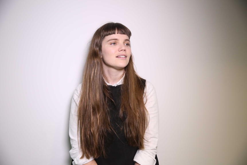 A portrait of a young woman with long brown hair wearing a white shirt with a black vest.