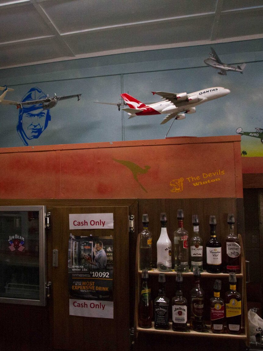 Model airplanes hang from the air above a bar with fridges and bottles of alcohol in a country town pub.
