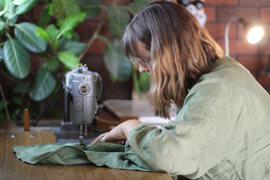 woman sewing zip into linen garment at old sewing machine 