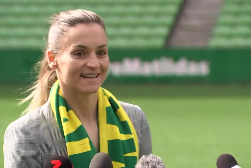 Melissa has a Matildas scarf around her neck and smiles at the tv camera on the AAMI Park pitch