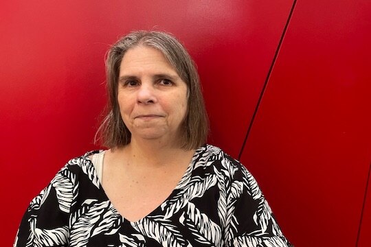 a woman with short grey hair sits in front of a red wall