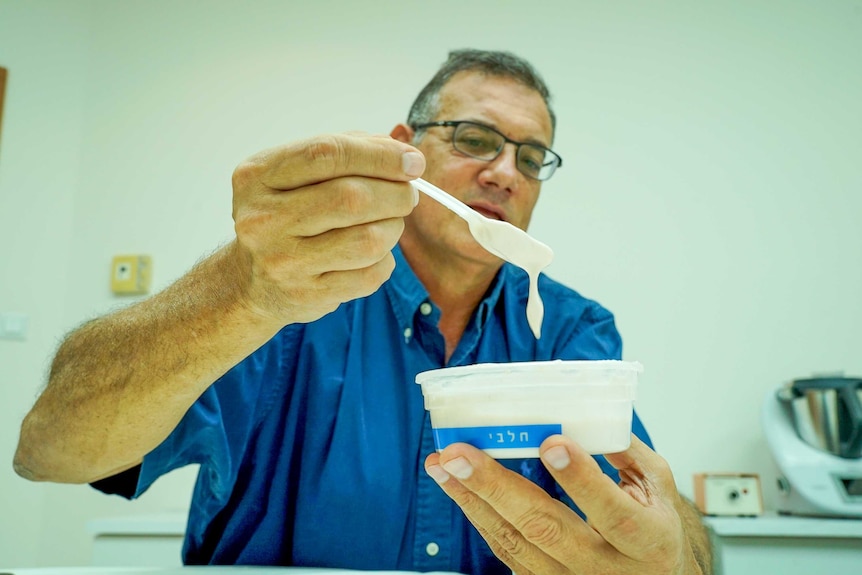 A man holds up a container of yoghurt with Hebrew writing on the side