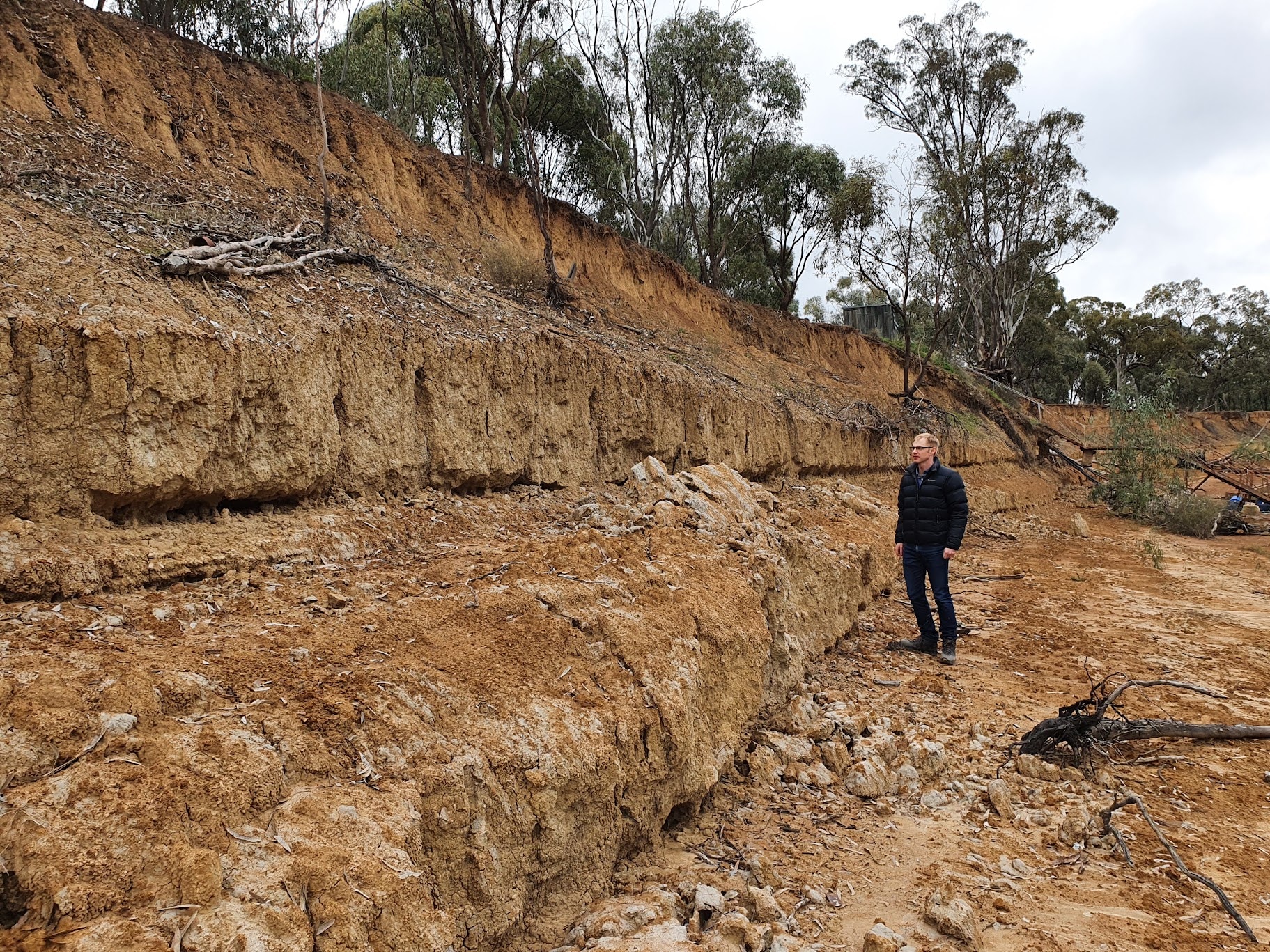 A man looks at a steep, dry riverbank twice his height