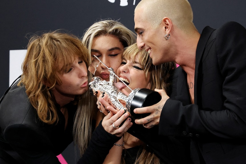 Four men and a woman kiss a trophy.