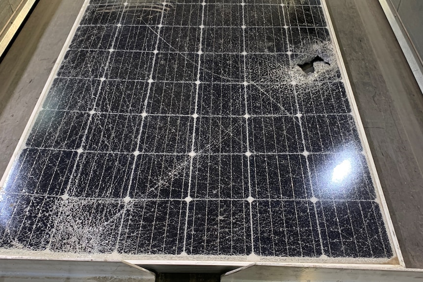 A solar panel on a conveyor belt that has been smashed, with cracks and a hole.