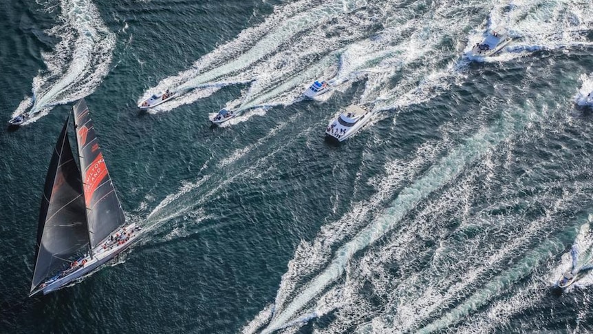Large sailboat with other watercraft in pursuit as seen from overhead.