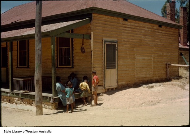 Tres niños se encuentran frente a una cabaña de madera. 