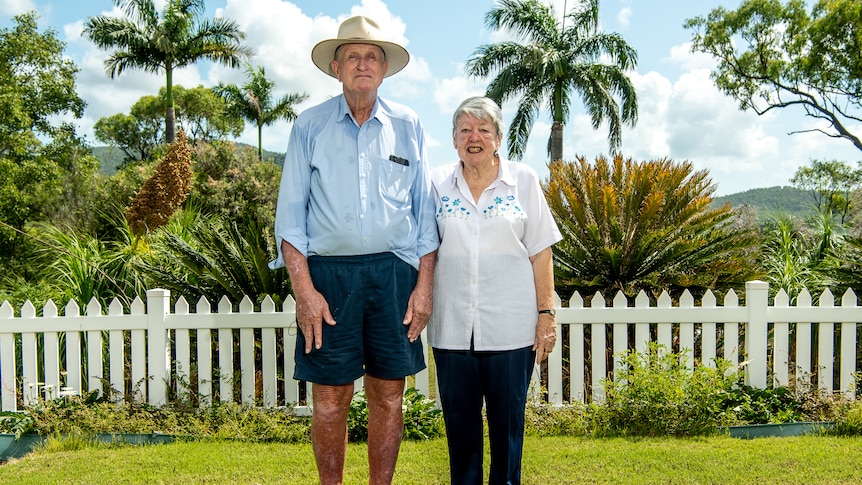 An elderly man and woman standing in a backyard with tropical plants 