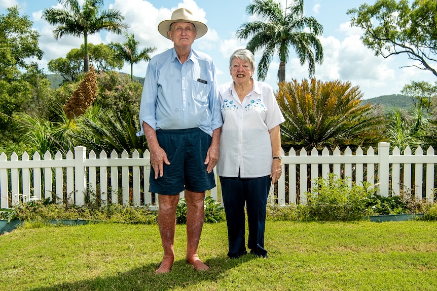 An elderly man and woman standing in a backyard with tropical plants 