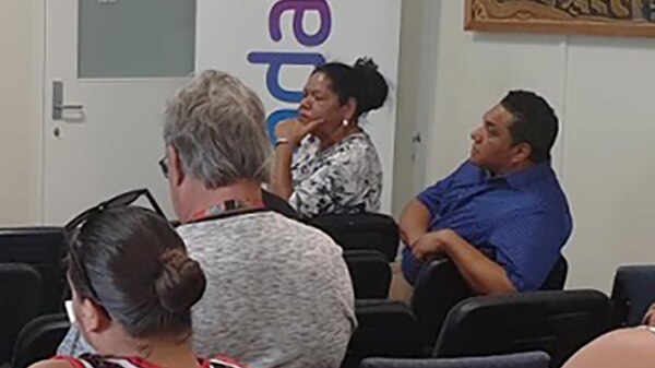 Irene Simpson, sits in a chair at the front of a room near Adani sign with hand under chin