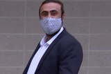 A man in a suit and a grey face mask walks outside a court building.