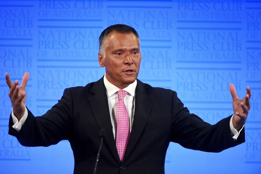 Stan Grant gestures with both hands as he speaks at the National Press Club podium.