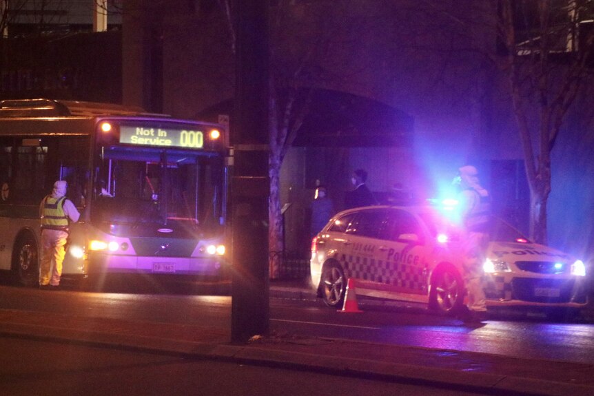 Samochód policyjny z migającymi światłami zaparkowany przed autobusem przed budynkiem.