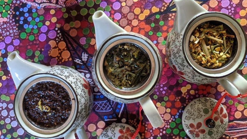 Three different tea blends in teapots sitting on a bright aboriginal art patterned tablecloth