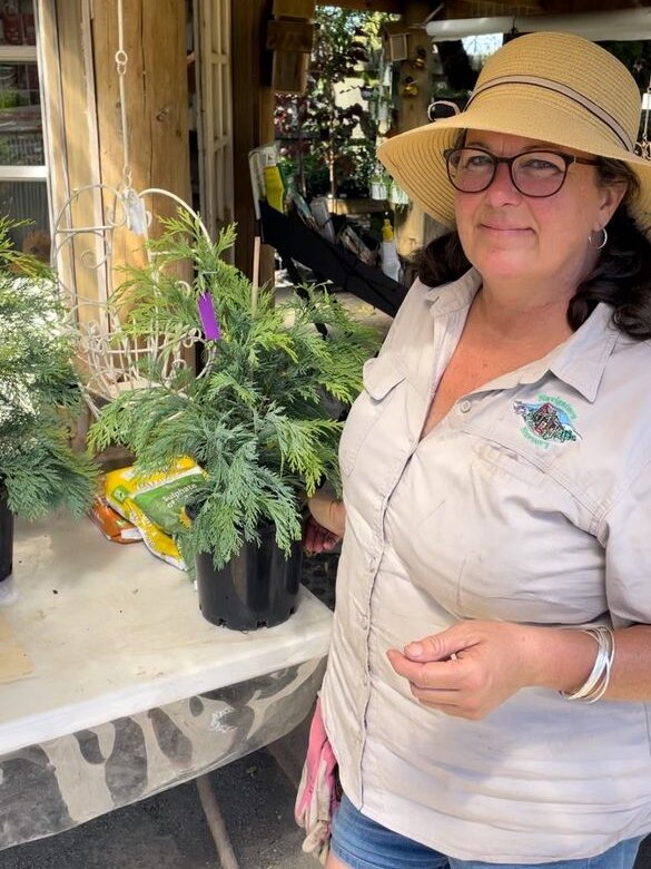 A woman wearing a hat stands in a plant nursery.