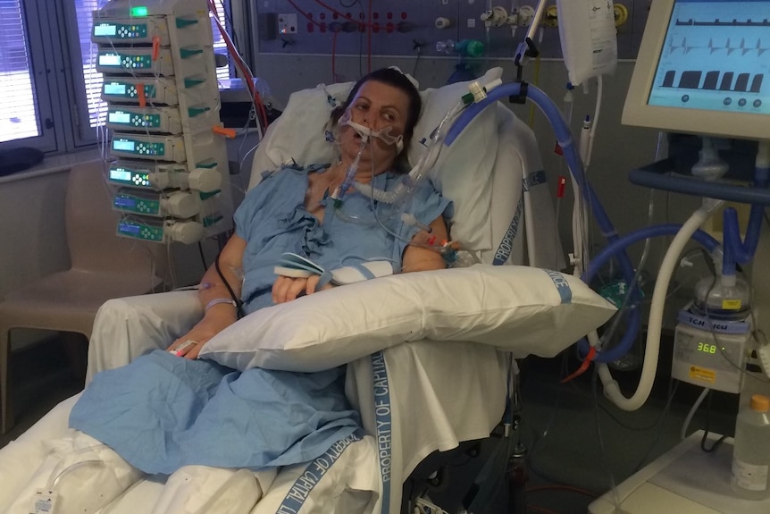 A woman in a blue gown on a ventilator in hospital.