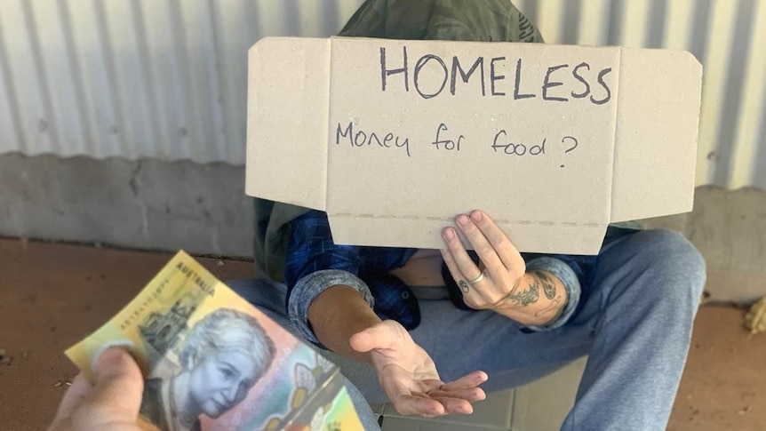一个人将一张 50 美元的钞票递给一个坐在地上举着“无家可归”标志的人