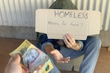A person hands a $50 note to a man sitting on the ground holding a 'homeless' sign